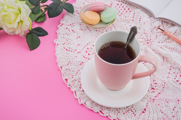 Pink tea cup with macaroons on lace tablecloth against pink background