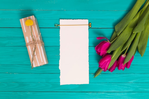 Pink tulip flowers; gift box; and blank white paper on green background