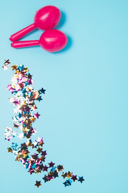 Free photo pink two maracas with colorful star shape confetti against blue background