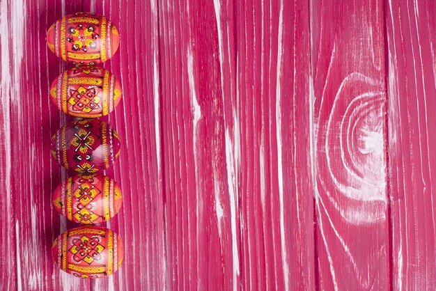 Pink wooden background with easter eggs in row