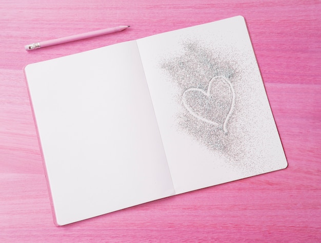 Pink wooden background with glitter notepad and heart