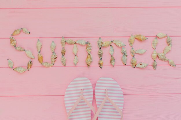 Pink wooden background with seashells and flip flops