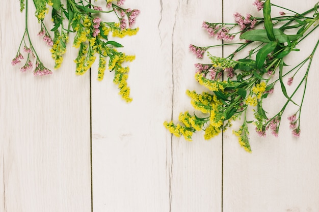 Розовые и желтые золотарники или солидаго гигантские цветы над деревянным столом