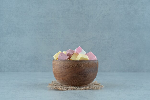 Pink and yellow marshmallow candies in a wooden bowl on white surface