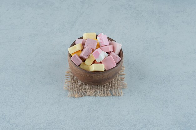 Pink and yellow marshmallow candies in a wooden bowl on white surface