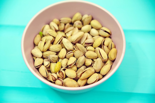 Pistachio nuts in pink bowl on blue wooden table background