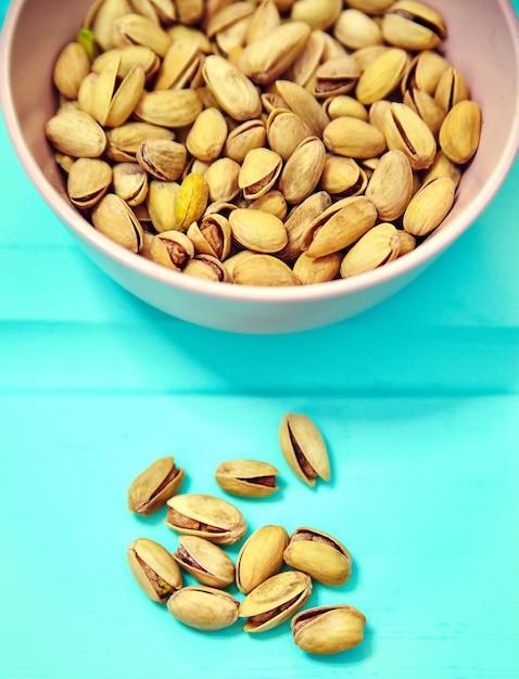 Pistachio nuts in pink bowl on blue wooden table background