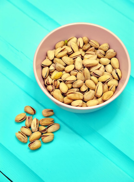 Pistachio nuts in pink bowl on blue wooden table background