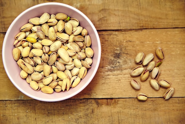 Free photo pistachio nuts in pink bowl on old wooden table background top view