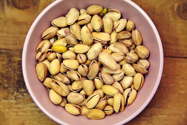 Pistachio nuts in pink bowl on old wooden table background Top view