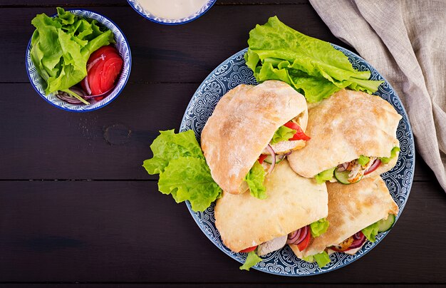 Pita stuffed with chicken, tomato and lettuce on wooden table. Middle Eastern cuisine. Top view