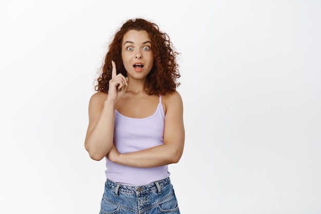 Pitching an idea Excited ginger girl redhead woman raising finger and gasp amazed telling solution think up great plan suggesting smth standing over white background