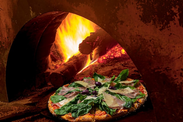 Pizza coming out of the wood oven. flavor: mozzarella  parma ham  parmesan cheese  arugula  black olives with oregano and sesame border. brazilian food