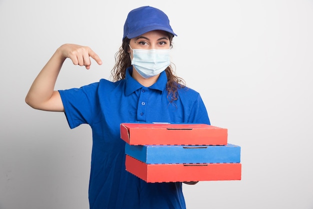Доставка пиццы держит три коробки с медицинской маской на белом