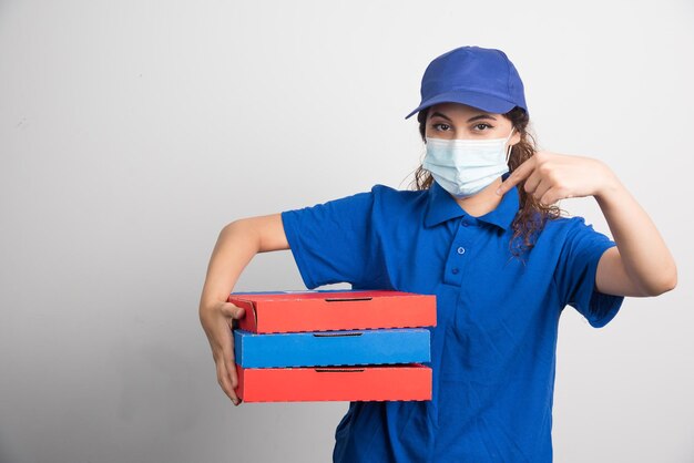 Pizza delivery girl holding three boxes with medical facemask on white