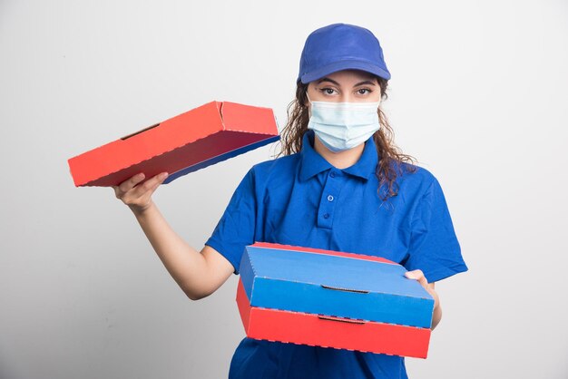 Pizza delivery girl holding three boxes with medical facemask on white