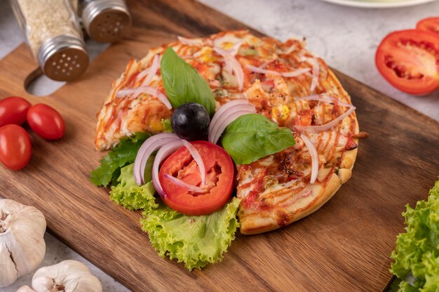 The pizza is in a wooden tray topped with red onions, black grapes, tomatoes, and lettuce.