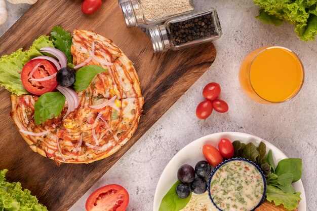 피자는 붉은 양파, 검은 포도, 토마토 및 양상추를 얹은 나무 쟁반에 있습니다.
