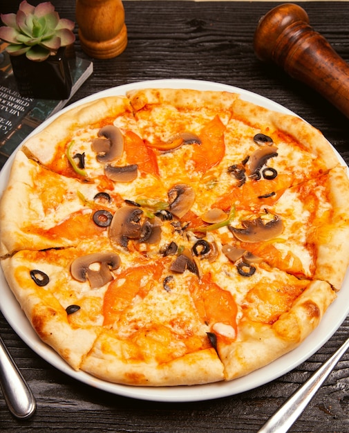 ブラックオリーブ、マッシュルーム、トマトソース、トマトのスライスとパルメザンチーズの白い皿の上のピザマルガリータ。