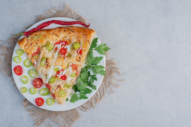 Pizza slice with peppers and parsley leaves on marble surface