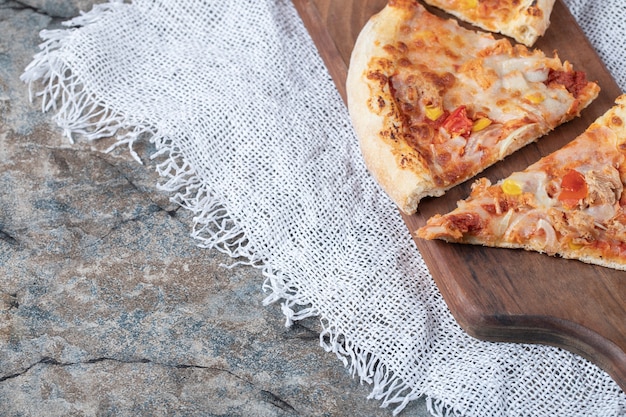Ломтики пиццы с плавленым сыром сверху на деревянной доске на куске белой мешковины