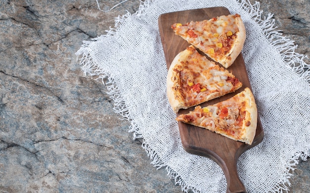 白い黄麻布の上に木の板の上に溶けたチーズが付いているピザのスライス