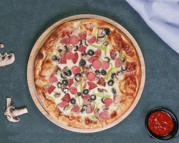 Pizza with chopped sausages, black olives and red chili sauce