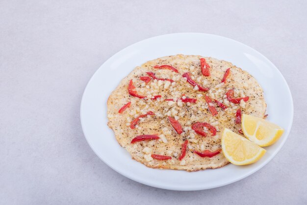 Pizza with peppers and half-cut lemon on white plate on white