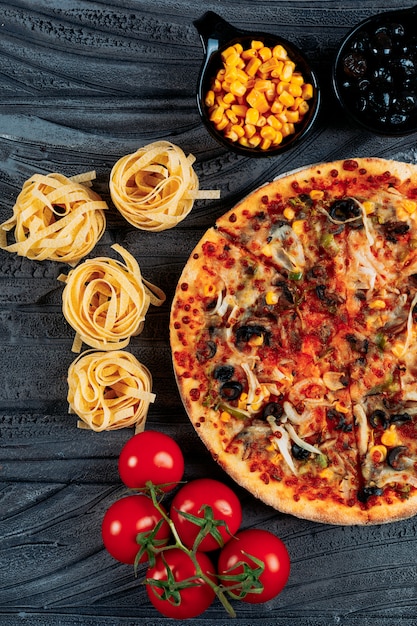 Pizza with spaghetti, tomatoes, olives, corn close-up on a dark blue background