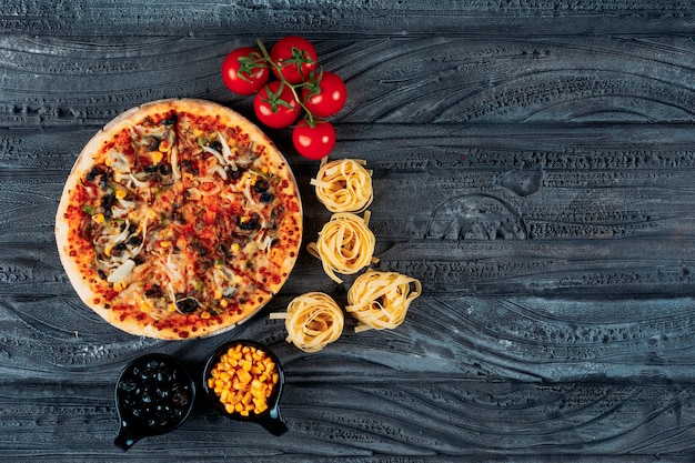 Pizza with spaghetti, tomatoes, olives, corn top view on a dark blue background