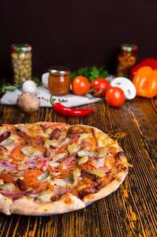 나무 테이블에 다양한 토핑과 치즈, 토마토, 버섯 및 기타 야채를 배경으로 하는 피자