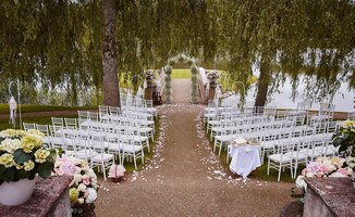 place for wedding ceremony with wedding arch decorated with flowers and white chairs on each side of archway outdoors. preparation for wedding ceremony outdoors near lake.
