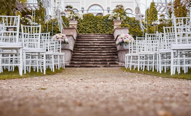 Luogo per la cerimonia di nozze con arco nuziale decorato con fiori e sedie bianche su ciascun lato dell'arco all'aperto. preparazione per la cerimonia di matrimonio all'aperto vicino al lago.