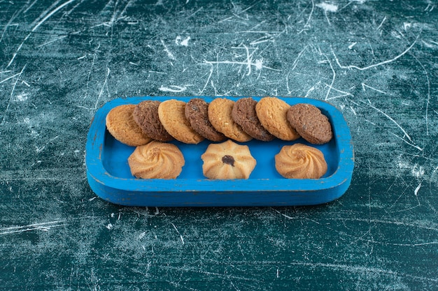 Foto gratuita biscotti semplici e al cioccolato su un vassoio di legno, sullo sfondo blu. foto di alta qualità