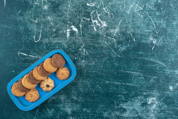 Plain and chocolate cookies on a wooden tray, on the blue surface