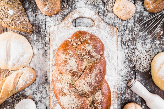 Plaited bread loaf on chopping board with flour over the table