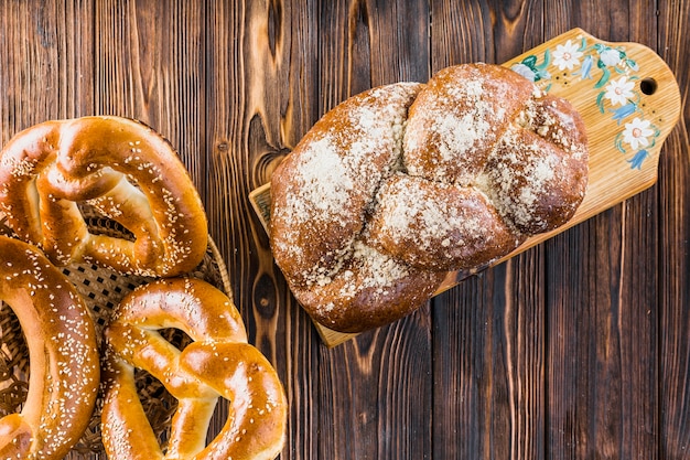 Free photo plaited loaf on chopping board and pretzels in basket over the table