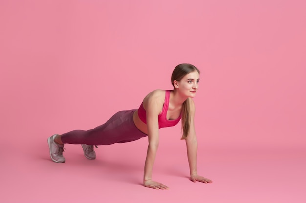 Plank balanced. Beautiful young female athlete practicing in studio, monochrome pink portrait. 