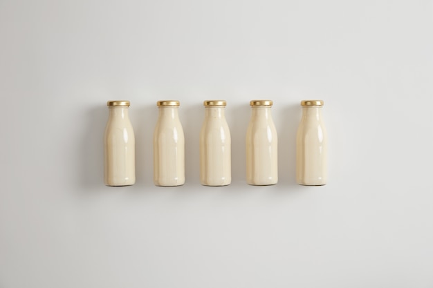 Plant based nut vegan milk in five glass bottles on white background. Vegetarian beverage as alternative to dairy product made of grains, legumes, nuts, seeds. Vegetable milk advertising concept