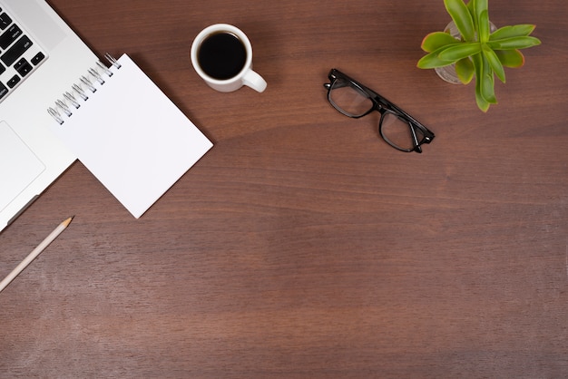 Free photo plant; eye glasses; tea; blank spiral notepad and pencil with laptop on wooden desk