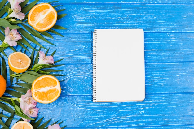 Plant leaves near oranges with blooms and notebook
