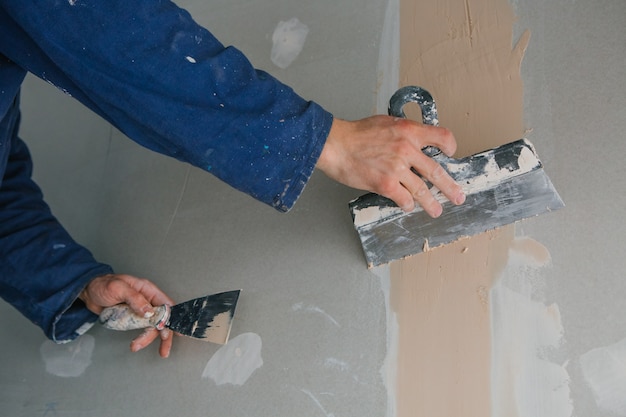 plasterer man works plastering two trowels on plasterboard in blue uniform