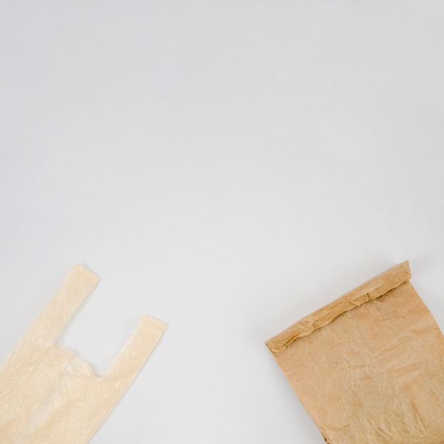 Free photo plastic bag and brown paper bag with copy space white backdrop