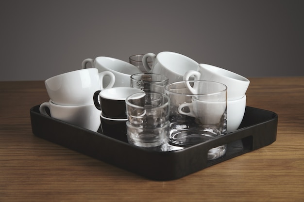 Plastic black salver with clean blank white coffee, tea, whiskey glasses and cups. on thick wooden table in cafe shop. Isolated on gray background.