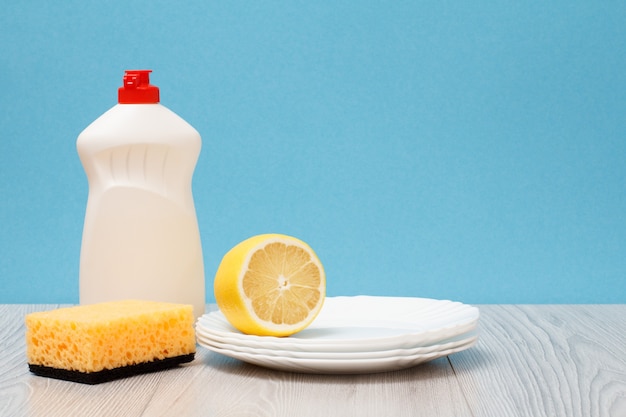 Пластиковая бутылка жидкости для мытья посуды, губка, чистые тарелки и лимон на синем фоне. концепция стирки и очистки.