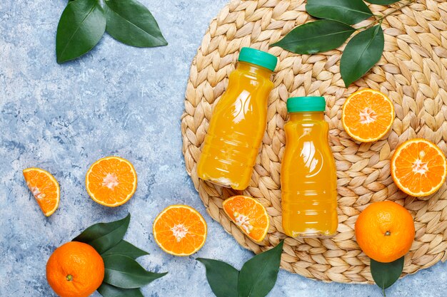 Plastic mini bottles of organic fresh orange juice with raw oranges and tangerines