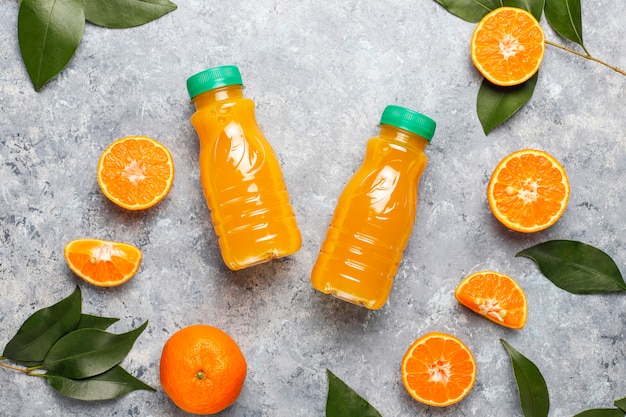 Plastic mini bottles of organic fresh orange juice with raw oranges and tangerines