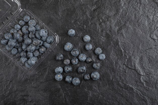 Plastic package of delicious fresh blueberries on black surface