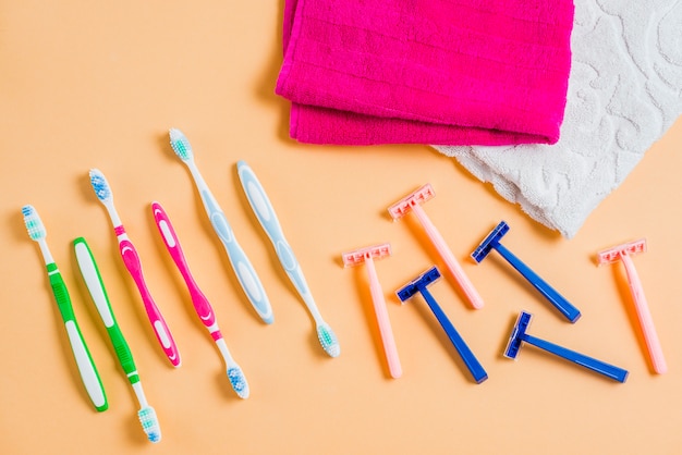 Plastic razor with tooth brushes and towel on colored background
