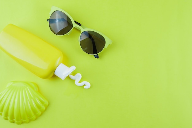 Plastic scallop; sunscreen lotion and sunglasses on green background